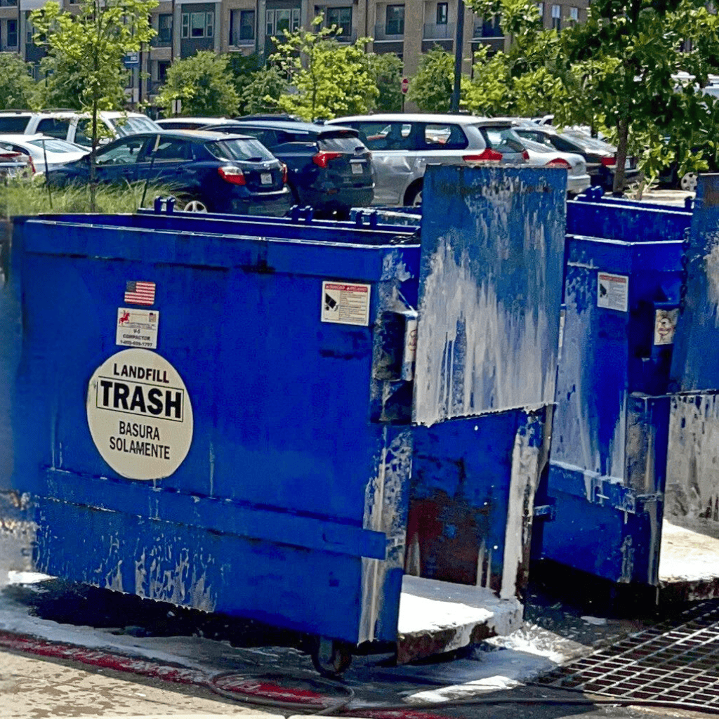 Blue commercial trash containers being cleaned with soap and water, showcasing the importance of professional trash can cleaning services for hygiene and curb appeal.
